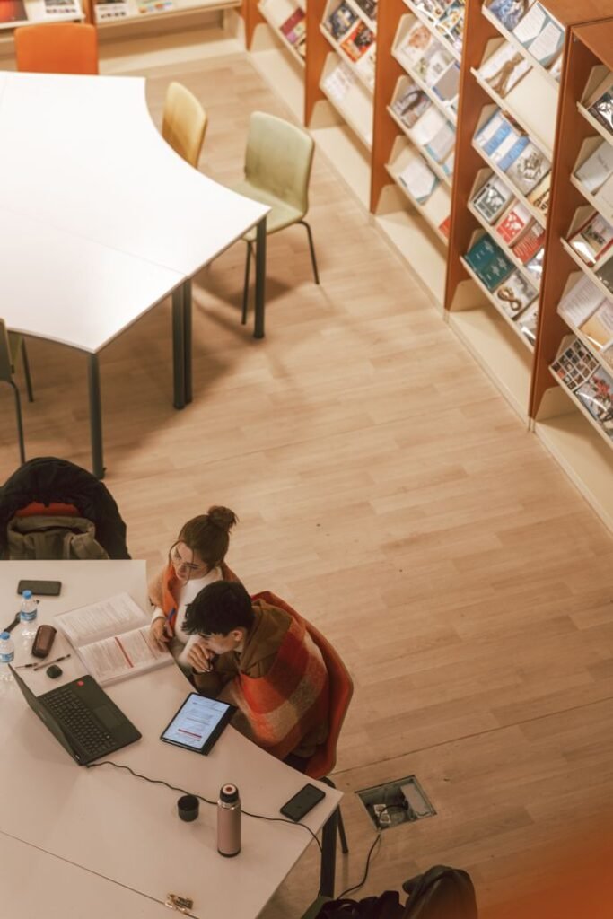Aerial view of a couple using a laptop and tablet while studying together in a library.